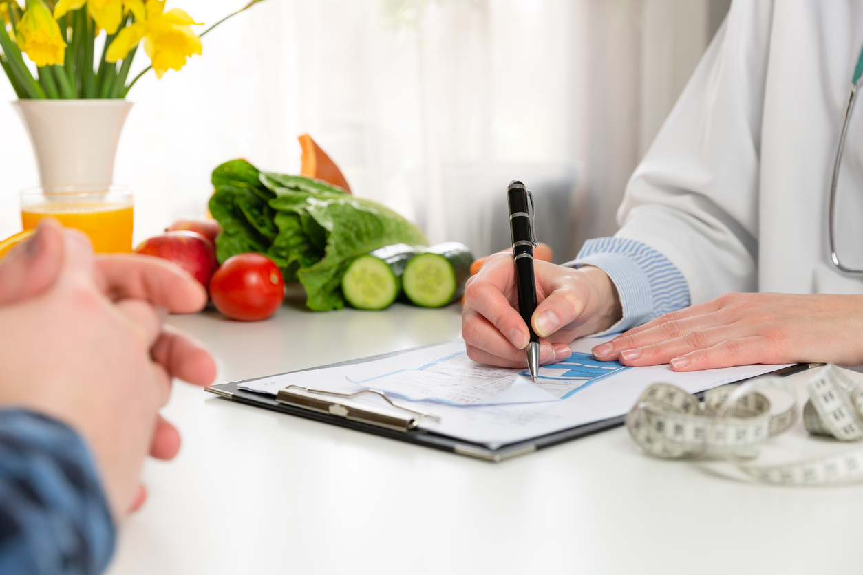 Nutrizionista che scrive un piano alimentare personalizzato con verdure fresche sul tavolo